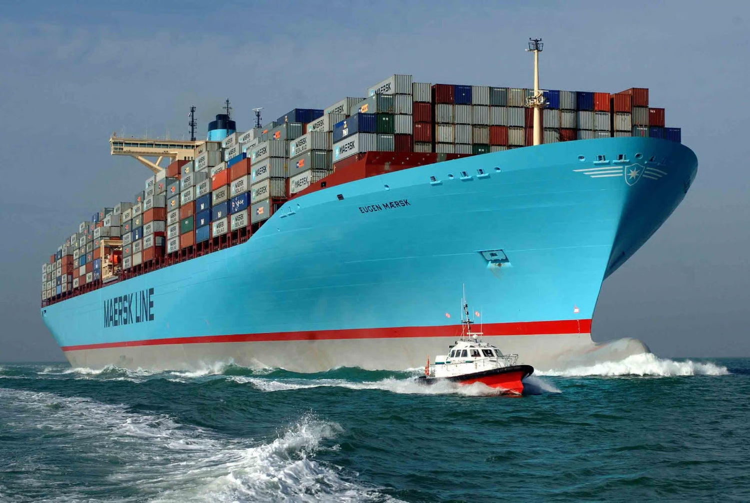 Large container ship with 'Maersk Line' branding sailing on the ocean, accompanied by a smaller boat.