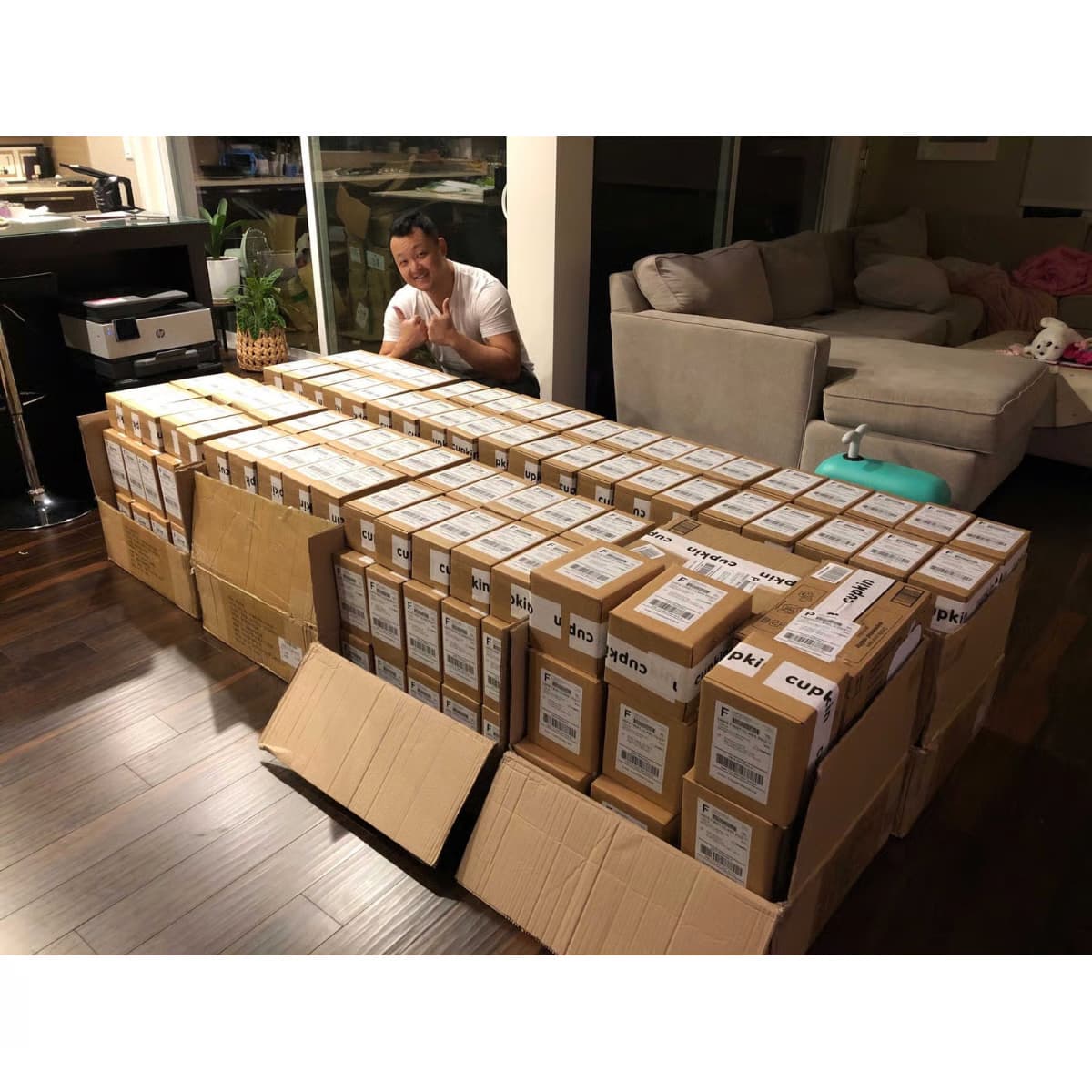 Man sitting behind a large number of stacked cardboard boxes in a living room.