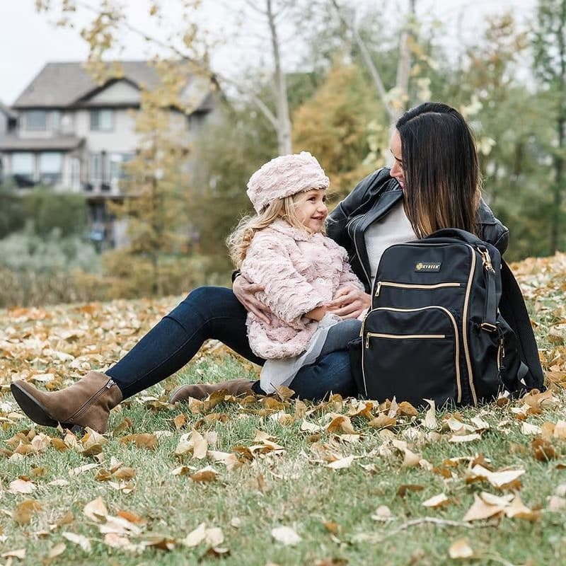 Woman and child sitting on grass with a backpack in an outdoor setting