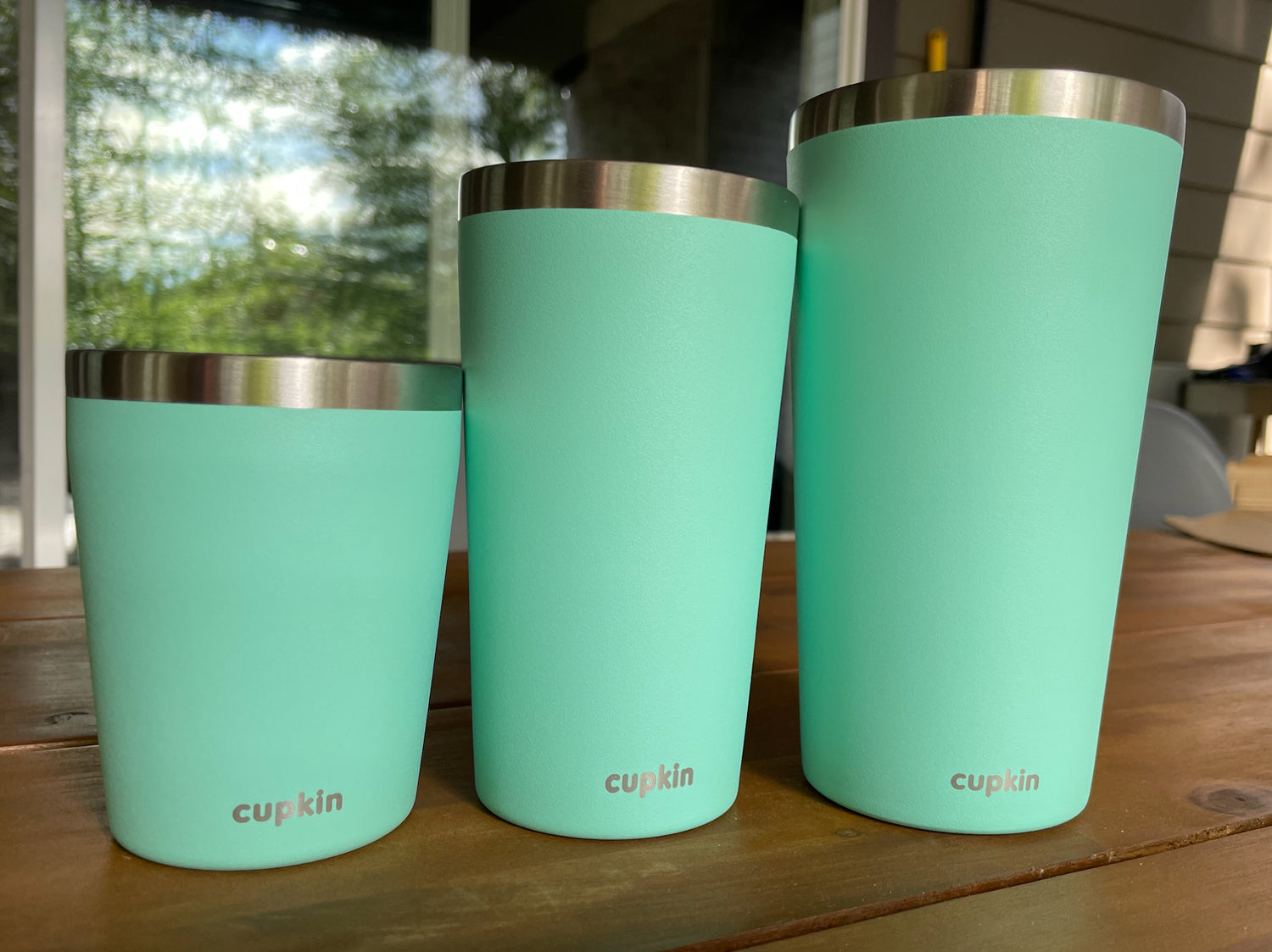 Three turquoise tumblers with silver lids on a wooden surface.