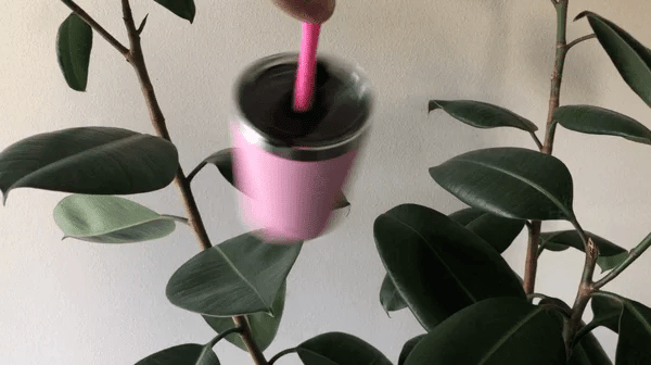 Pink cup with straw held above a plant