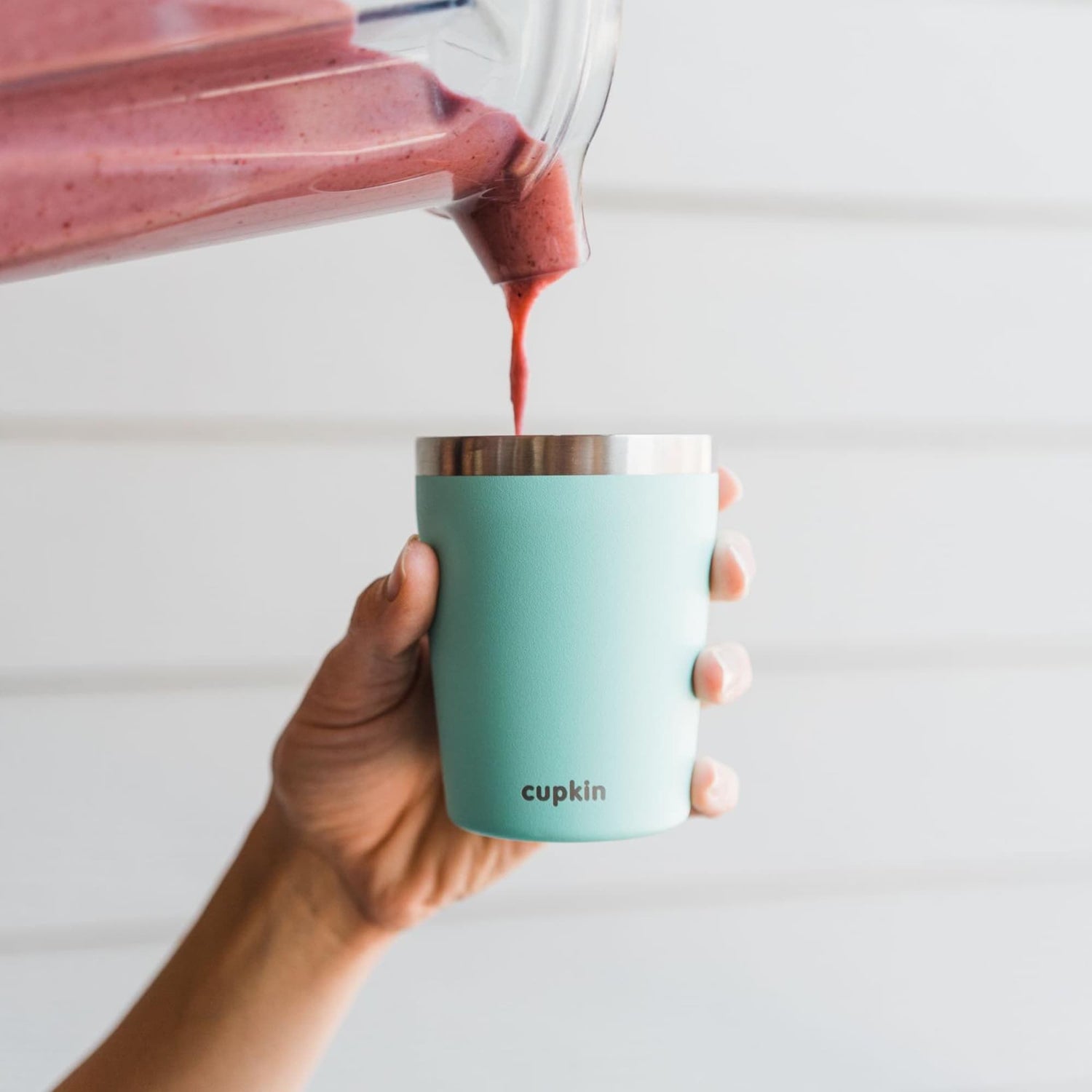 Red smoothie being poured from a blender into a teal Cupkin cup.